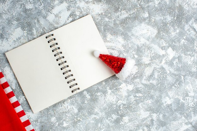 Juguete del sombrero de Navidad del cuaderno de la vista superior en el espacio libre de la mesa blanca gris