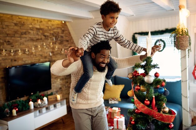 Juguetón padre afroamericano e hijo divirtiéndose en Navidad en casa