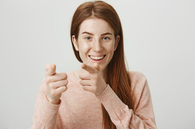 Juguetona chica pelirroja sonriente señalando con el dedo, te felicito