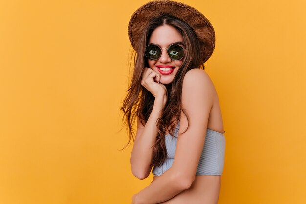 Juguetona chica de pelo largo posando con una sonrisa interesada mientras está sentada en el espacio amarillo