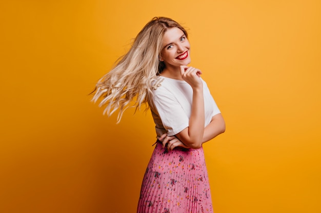 Juguetona chica rubia expresando felicidad. dama elegante refinada escalofriante en la pared naranja.