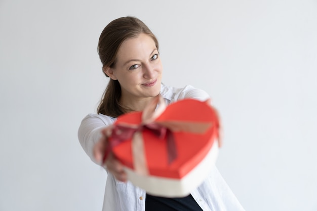 Juguetona mujer muy joven dando caja de regalo en forma de corazón