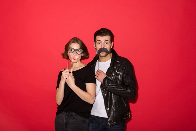 Juguetona pareja punk posando con bigote falso, labios y anteojos