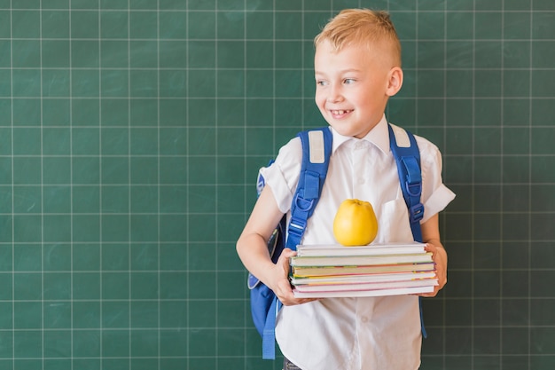 Foto gratuita junior con mochila y libros de texto cerca de la pizarra