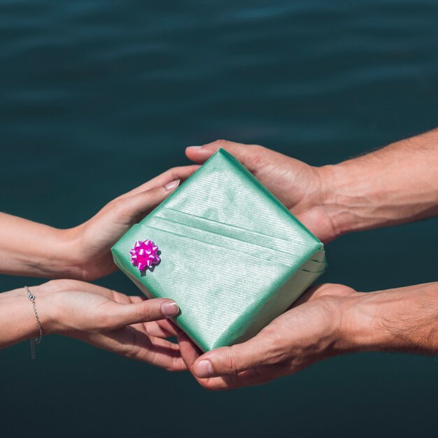 Junte sostener la caja de regalo verde delante del fondo del agua de mar