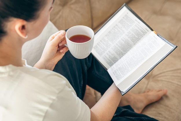 Foto gratuita junto a una mujer joven bebiendo té caliente y leyendo su libro de papel favorito