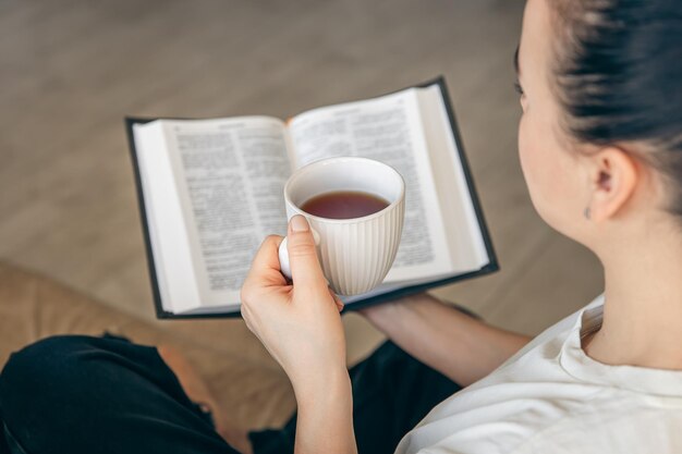 Junto a una mujer joven bebiendo té caliente y leyendo su libro de papel favorito