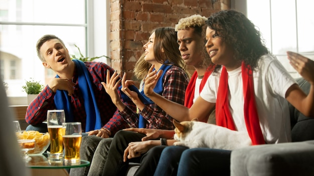 Juntos. Gente emocionada viendo partido deportivo, campeonato en casa. Grupo multiétnico de amigos, fanáticos animando al equipo deportivo favorito