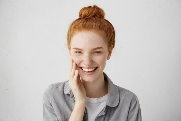 Juventud y felicidad. Vista de cerca de la hermosa mujer adolescente caucásica con pelo largo de jengibre y pecas, vestida informalmente, de pie contra la pared gris en blanco.