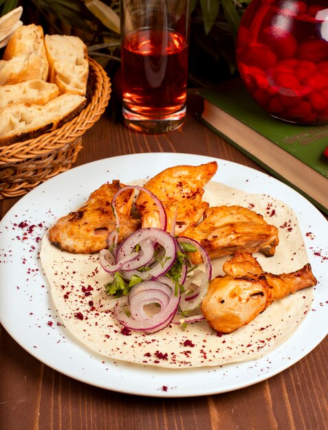 Kebab de alitas de pollo a la parrilla servido con composto, ensalada de cebolla y hierbas en un plato blanco