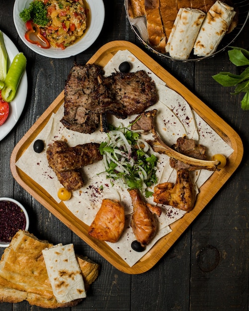 Kebab de carne caucásica con ensalada de cebolla a base de hierbas dentro de una bandeja de madera.