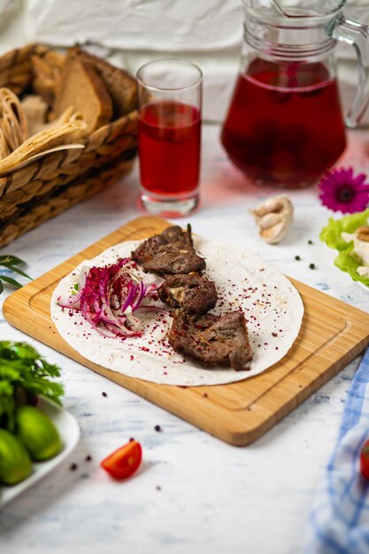 Kebab de carne de res con cebolla, sumakh y lavash en un plato de madera servido con vino y verduras