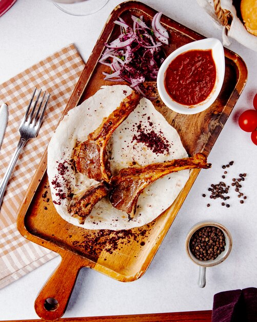 Kebab de costillas de cordero con cebolla roja sobre una plancha de madera