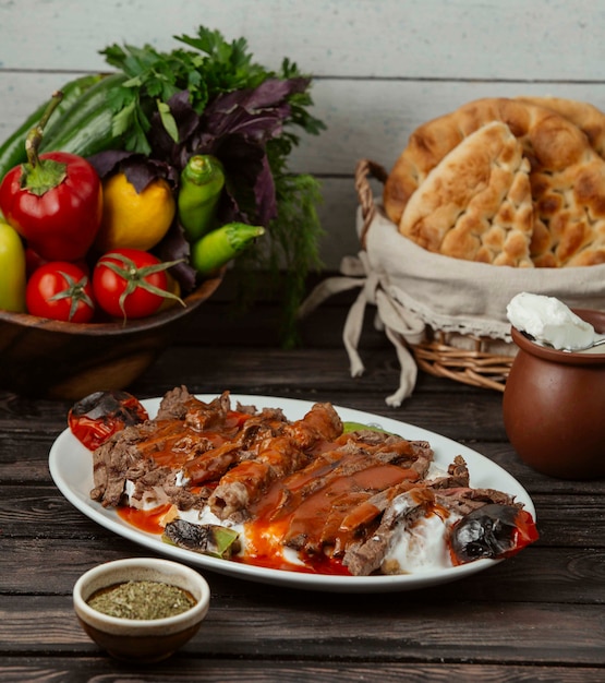 Kebab de Iskender adornado con salsa de tomate y yogur, servido con verduras a la parrilla