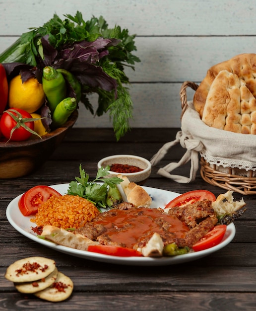 Kebab de ternera adornado con rodaja de tomate, servido con bulgur, pan y verduras