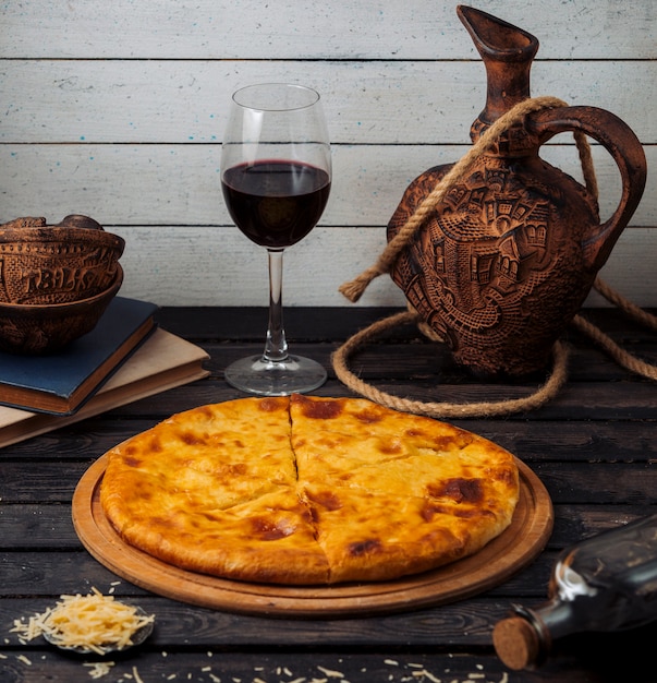 Foto gratuita khachapuri georgiano servido sobre tabla de pizza de madera con vino tinto