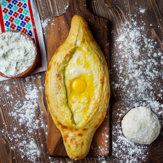 Khachapuri con papel de cocina, masa, harina en madera y tabla de cortar