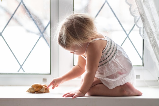 Kid juega con un gran caracol en la ventana real estilo de vida interior softfokus el concepto de infancia y animales