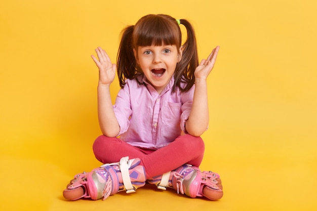 Kid niña en patines se sienta en el suelo en texto libre