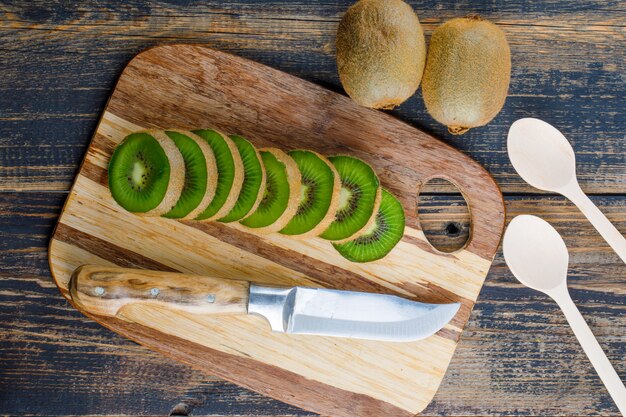 Kiwi fresco con cuchillo, cucharas planas sobre fondo de madera y tabla de cortar