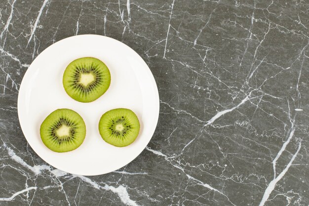 Kiwi en rodajas en un plato blanco sobre piedra negra.