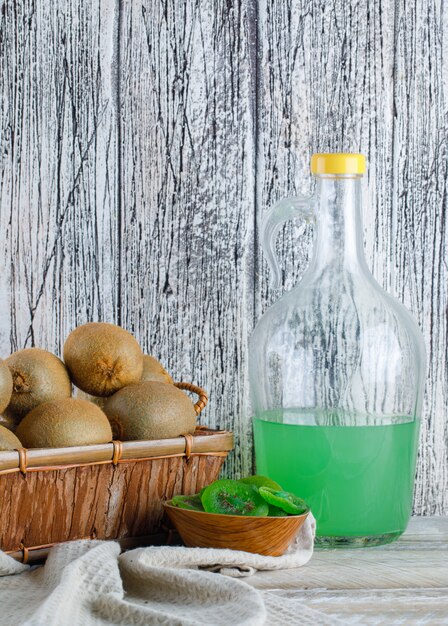 Kiwi con rodajas secas, jugo en una cesta en madera y papel de cocina, vista lateral.