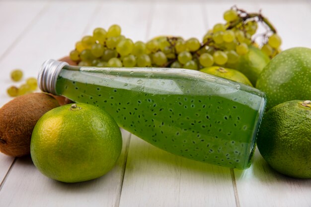 Kiwi de vista frontal con una botella de jugo de uvas y mandarinas en una pared blanca