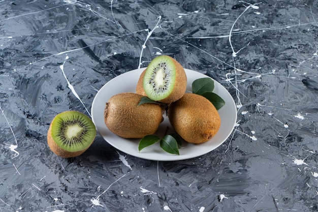 Kiwis enteros y en rodajas con hojas colocadas en un plato blanco.