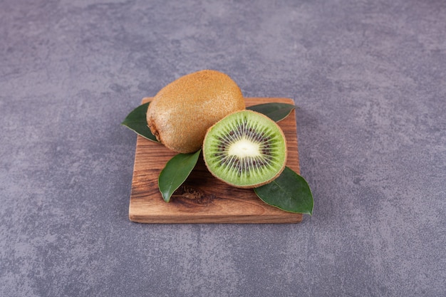 Kiwis enteros y en rodajas con hojas colocadas sobre una piedra.