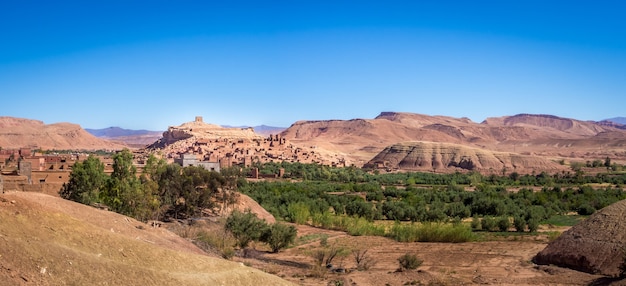 Ksar de Ait-Ben-Haddou rodeado de vegetación bajo la luz del sol y un cielo azul en Marruecos