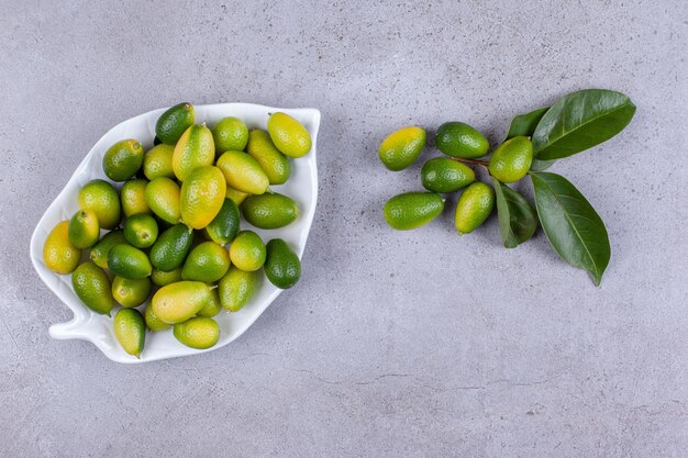 Kumquats en bandeja con un puñado junto a hojas sobre fondo de mármol. Foto de alta calidad