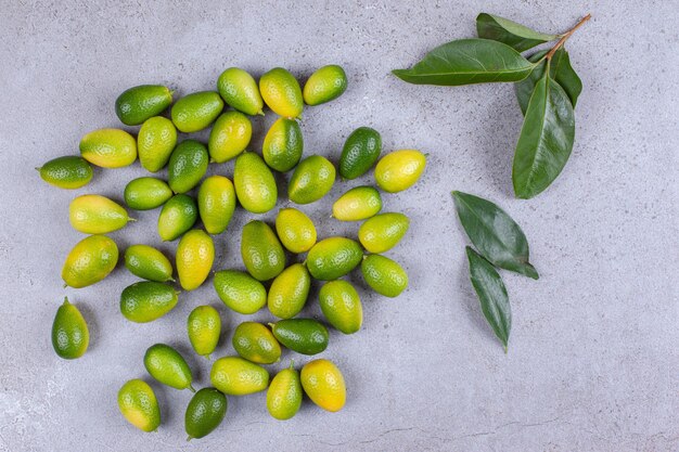 Kumquats esparcidos y hojas sobre superficie de mármol.