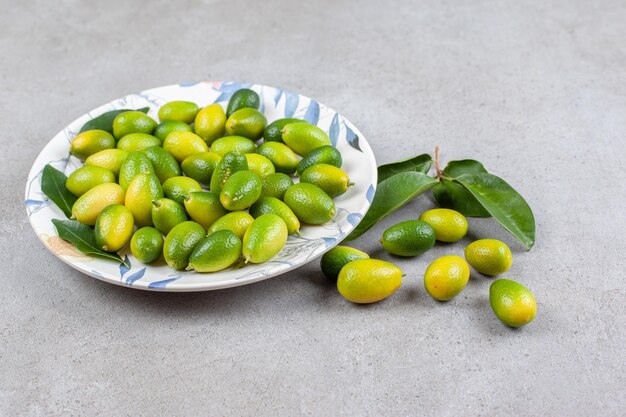 Kumquats y hojas sobre un plato adornado y sobre superficie de mármol.