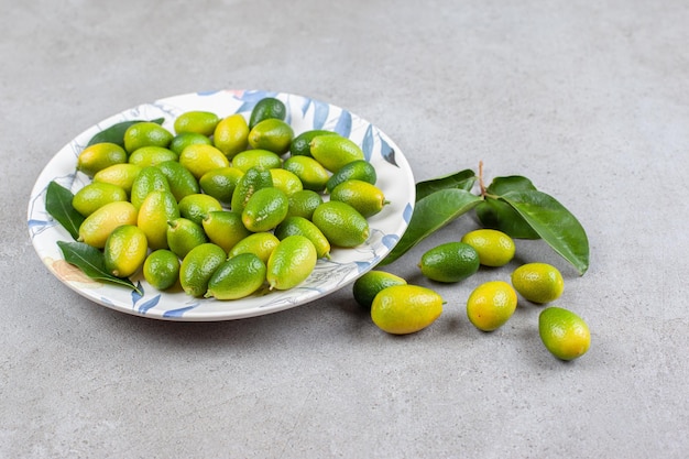 Kumquats y hojas sobre un plato adornado y sobre superficie de mármol.