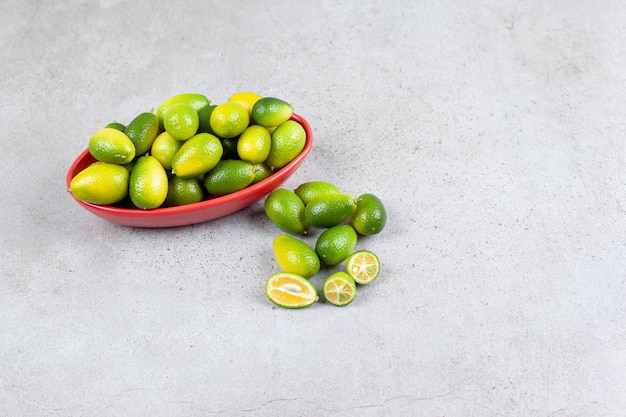 Kumquats inmaduros amontonados y junto a un tazón con algunos cortados en rodajas sobre la superficie de mármol