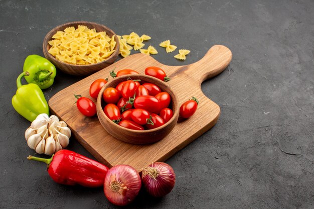 Lado de cerca pasta pasta cebolla pimiento junto a los tomates en un tazón en la tabla de madera sobre la mesa