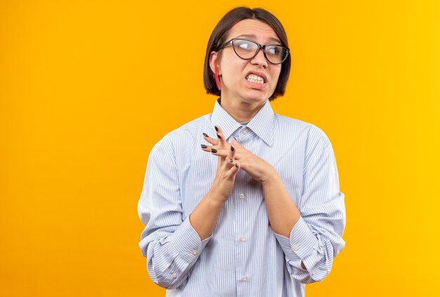 Lado de mirada disgustado hermosa joven con gafas cogidos de la mano juntos aislado en la pared naranja