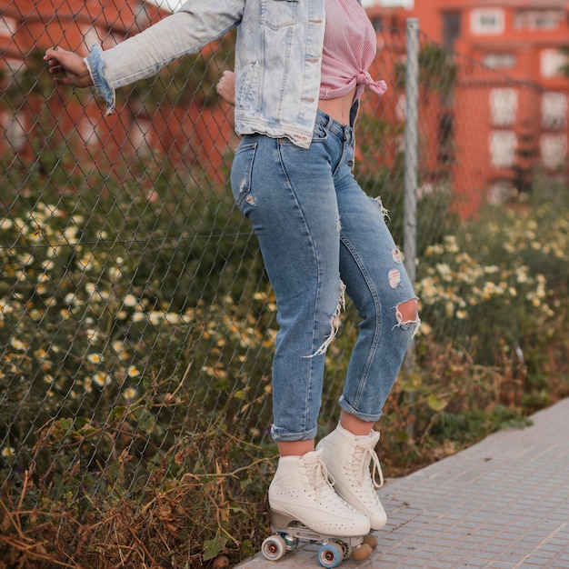 Foto gratuita lado de la mujer joven que lleva el patín de ruedas de pie cerca de la valla