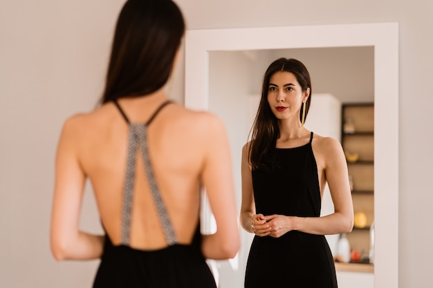 Lady lleva un hermoso vestido negro mirándose al espejo