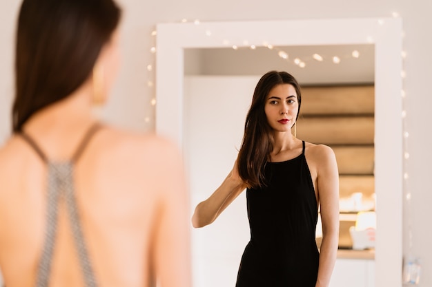 Lady lleva un hermoso vestido negro mirándose al espejo