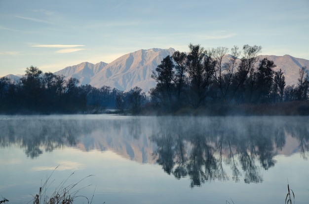 Lago escénico con reflejo de montañas y árboles bajo un cielo azul