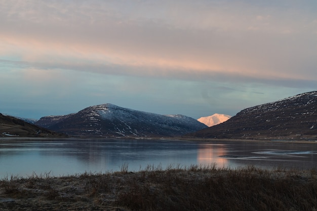 Lago rodeado por colinas cubiertas de nieve que se refleja en el agua durante la puesta de sol en Islandia