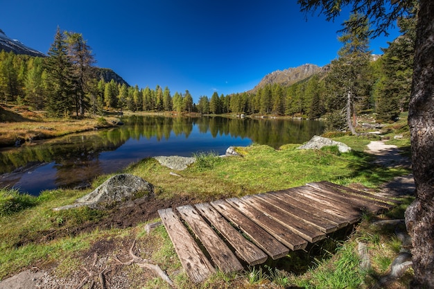 Lago rodeado de rocas y un bosque con árboles reflejándose en el agua bajo un cielo azul en Italia