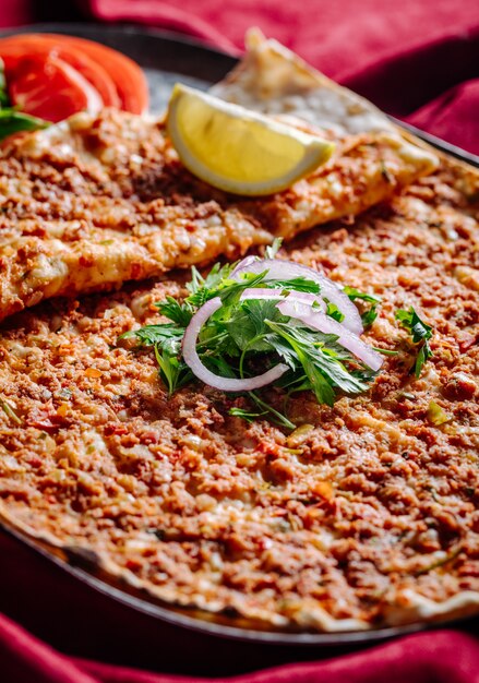 Lahmacun con relleno de carne servido con cebolla picada, perejil, tomate y limón.