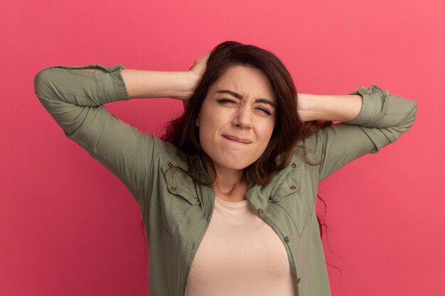 Lamentado con los ojos cerrados joven hermosa vestida con camiseta verde oliva agarró la cabeza aislada en la pared rosa