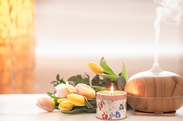 Lámpara difusora de aceite aromático sobre la mesa borrosa con un hermoso ramo primaveral de tulipanes y velas encendidas.