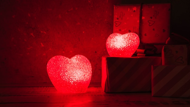 Lámparas iluminadas en forma de corazones cerca de cajas de regalo.
