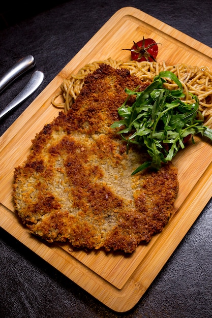 Langet de carne sobre la plancha de madera con espaguetis rúcula tomate vista lateral