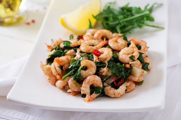 Langostinos fritos o gambas con espinacas, chile y ajo en plato blanco.