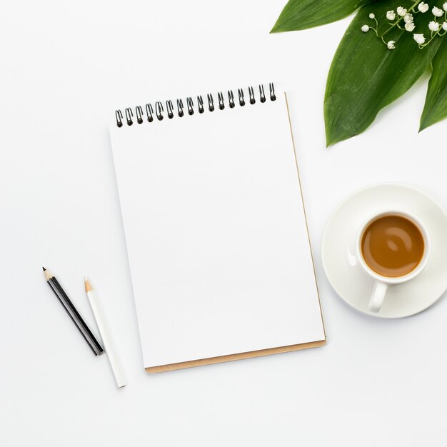 Lápices de colores en blanco y negro, bloc de notas en espiral, taza de café y hojas en el escritorio de oficina